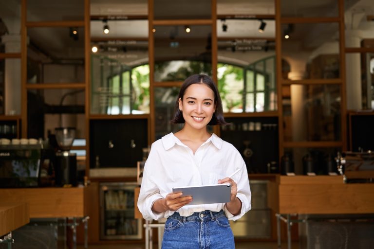 Portrait of asian woman, manager standing with tablet in front of cafe entrance, welcomes guests Portrait of asian woman, manager standing with tablet in front of cafe entrance, welcomes guests